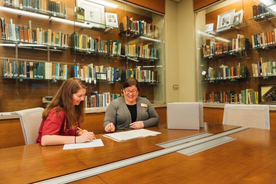 Oxford Library archivist meeting with a student, sitting at a table looking over a shared document. 