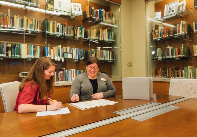 Librarian assisting a student at a table in the Special Collections room.